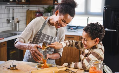 A Practical Guide to Recharging this Holiday Season. Son is helping mother to prepare pumpkin pie. American family. Single mother. Household chores for kids.